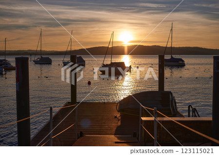 A serene sunset over a calm river, with vibrant orange and pink hues in the sky. A small sailboat is anchored in the water, reflecting the colorful sky. 123115021