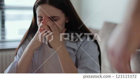 Young woman sitting on sofa, looks pessimistic and sad, almost crying, man calming her down, softly touches and hugs her. Partnership and support concept. Young woman sitting on sofa, looks pessimistic and sad, almost crying, man calming her down, softly touches and hugs her. Partnership and support concept. 123115372