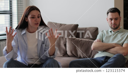 Couple sitting on sofa in living room arguing over disagreement, woman yelling at man, man experiencing psychological abuse from his wife. Relationship crisis. Couple sitting on sofa in living room arguing over disagreement, woman yelling at man, man experiencing psychological abuse from his wife. Relationship crisis. 123115374