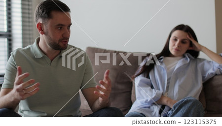 Couple sitting on sofa in living room arguing over disagreement, man yelling at woman, woman experiencing psychological abuse from her husband. Couple sitting on sofa in living room arguing over disagreement, man yelling at woman, woman experiencing psychological abuse from her husband. 123115375