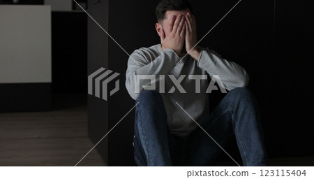 Sad man sitting in the dark leaning against the wall in home. Family problems, stress. 123115404