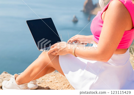 A woman is sitting on a rock by the water with a laptop open in front of her. She is typing on the laptop and she is focused on her work. Concept of productivity and concentration. A woman is sitting on a rock by the water with a laptop open in front of her. She is typing on the laptop and she is focused on her work. Concept of productivity and concentration. 123115429