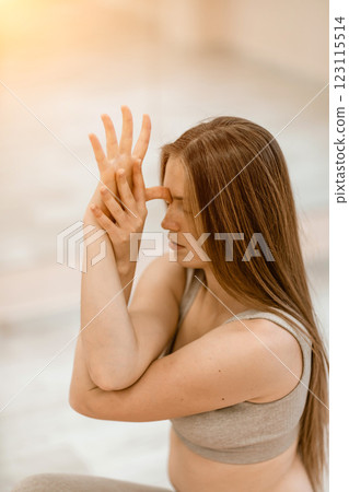 Young woman doing yoga in the gym. A girl with long hair and in a beige tracksuit stands in a cow pose on a pink carpet. A woman performs Gomukhasana. Young woman doing yoga in the gym. A girl with long hair and in a beige tracksuit stands in a cow pose on a pink carpet. A woman performs Gomukhasana. 123115514