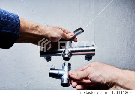 Two hands hold parts of disassembled mixer tap, including main body and diverter valve with visible threading for installation. 123115862