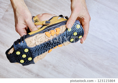 Ice grippers with yellow metal spikes and rubber base are securely fitted to hiking boot for stability on icy terrain. Ice grippers with yellow metal spikes and rubber base are securely fitted to hiking boot for stability on icy terrain. 123115864