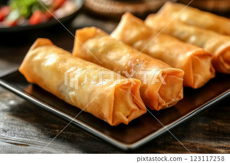 Close-up of crispy spring rolls served on black plate with fresh vegetables at dining table Close-up of crispy spring rolls served on black plate with fresh vegetables at dining table 123117258