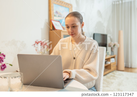 Young woman working on a laptop at home. Concept of remote work, education, and digital communication. Flexible hybrid work and learning conditions. Young woman working on a laptop at home. Concept of remote work, education, and digital communication. Flexible hybrid work and learning conditions. 123117347