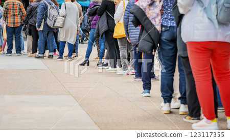 People standing in a long queue outdoors on city street. Public crowd. Women and men stand behind each other. Consumerism, waiting concept 123117355