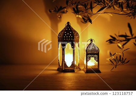 Two Moroccan lanterns on table at nigh. Blurred olive tree branches. Golden glow. Festive banner, invitation for Muslim holiday Ramadan Kareem. Eid mubarak celebration. Religion concept, copy space. Two Moroccan lanterns on table at nigh. Blurred olive tree branches. Golden glow. Festive banner, invitation for Muslim holiday Ramadan Kareem. Eid mubarak celebration. Religion concept, copy space. 123118757