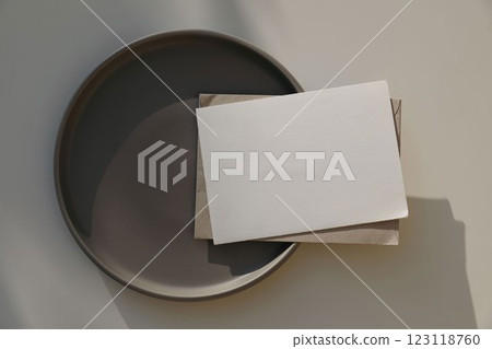 Empty greeting card, invitation mockup, craft envelope in sunlight on brown ceramic plate. Beige table background. Neutral web banner. Elegant minimal wedding, birthday template. Flat lay, top view. Empty greeting card, invitation mockup, craft envelope in sunlight on brown ceramic plate. Beige table background. Neutral web banner. Elegant minimal wedding, birthday template. Flat lay, top view. 123118760