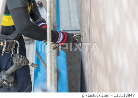 [Large-scale apartment building repair work: Workers connecting wall ties and building scaffolding] 123118947