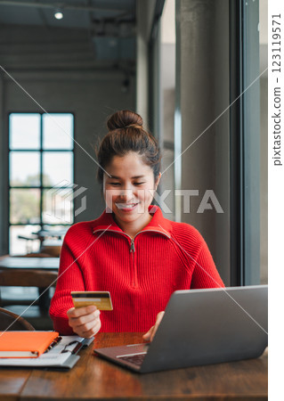Smiling woman in red sweater using laptop and credit card for online shopping in a modern cafe. Smiling woman in red sweater using laptop and credit card for online shopping in a modern cafe. 123119571