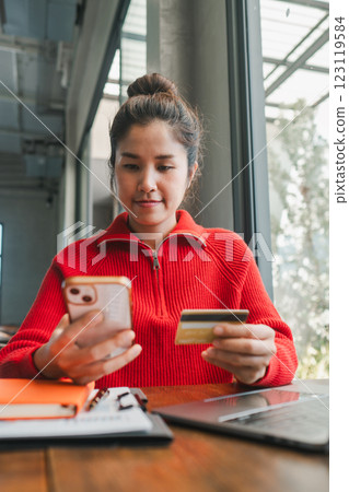 Woman in red sweater using smartphone and credit card for online shopping in a cafe with natural light. Woman in red sweater using smartphone and credit card for online shopping in a cafe with natural light. 123119584