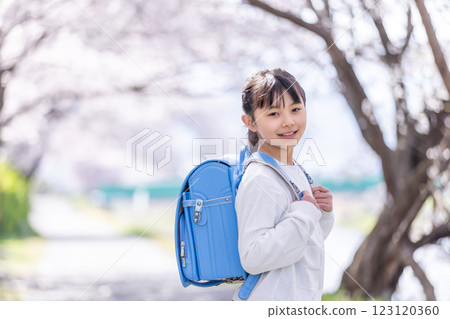 A girl smiling under a cherry tree with a school bag on her back 123120360