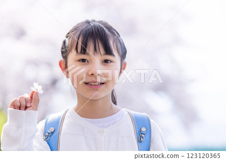 A girl smiling under a cherry tree with a school bag on her back A girl smiling under a cherry tree with a school bag on her back 123120365