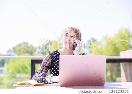 A woman smiling and talking on the phone with her laptop open A woman smiling and talking on the phone with her laptop open 123123291