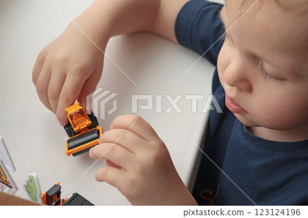 Little curly-haired blond boy playing with car on white table. Development games for children.  123124196