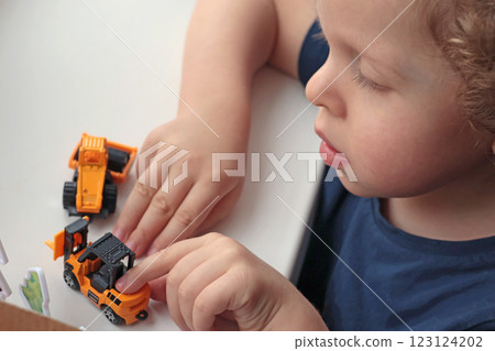 Little curly-haired blond boy playing with car on white table. Development games for children. Little curly-haired blond boy playing with car on white table. Development games for children. 123124202
