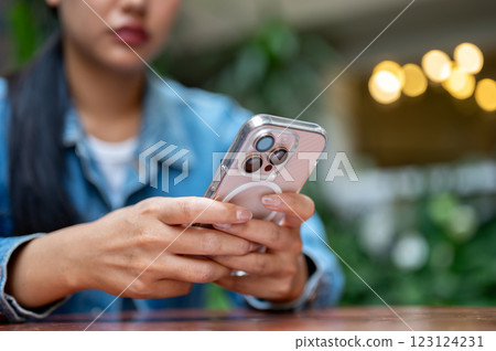 The close up shot of a woman, with face half hiding, holding a pink smartphone on the wooden tabletop. The close up shot of a woman, with face half hiding, holding a pink smartphone on the wooden tabletop. 123124231