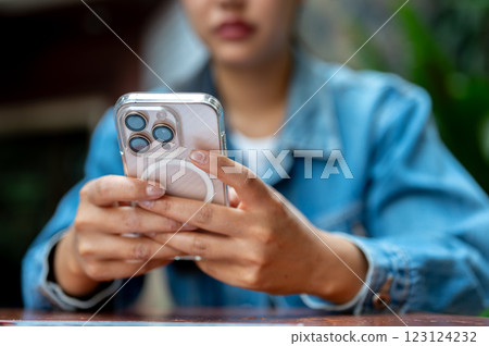 The close up shot of woman hand in denim jacket holding a smartphone, sitting on wooden table. The close up shot of woman hand in denim jacket holding a smartphone, sitting on wooden table. 123124232