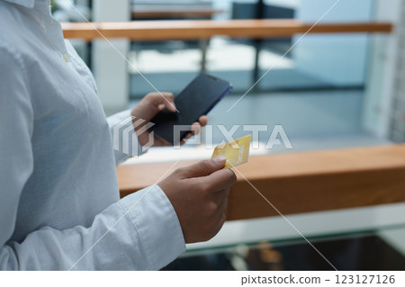 Person holding smartphone and credit card indoors in a modern space, exploring digital payment options and transactions 123127126