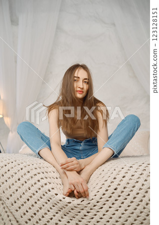 Young woman sitting comfortably on bed with a relaxed pose in a cozy room Young woman sitting comfortably on bed with a relaxed pose in a cozy room 123128151