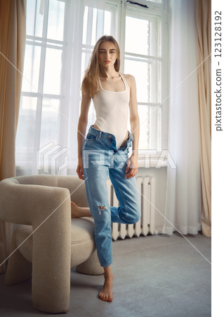 A barefoot woman stands near a stylish chair in a bright living room A barefoot woman stands near a stylish chair in a bright living room 123128192