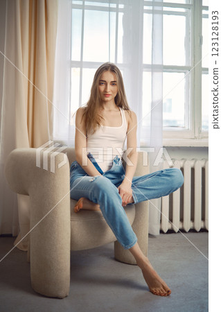 Woman sitting in a comfortable chair by a window in a bright indoor space 123128193