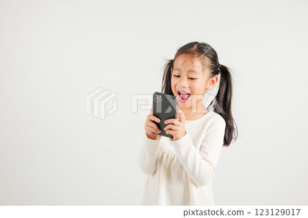Happy Asian portrait cute young kid girl smiling excited using smart mobile phone studio isolated on white background, Thai kindergarten child surprised holding reading message gesture on smartphone 123129017