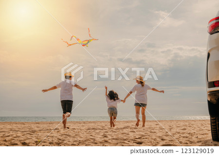 Asian family is flying a kite while running on the beach. Happy parents mother and father with their child playing with kite, The car is parked nearby, and the family is enjoying their time together 123129019