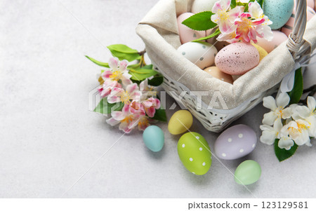 Pastel colored easter eggs overflowing from a white wicker basket decorated with spring flowers 123129581