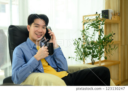 Smiling man enjoying a coffee and talking on the phone in a cozy home Smiling man enjoying a coffee and talking on the phone in a cozy home 123130247