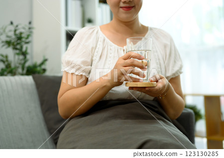 Smiling adult woman sitting on a couch and holding a glass of water Smiling adult woman sitting on a couch and holding a glass of water 123130285