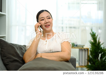 Middle aged woman having phone conversation sitting in bright living room 123130286