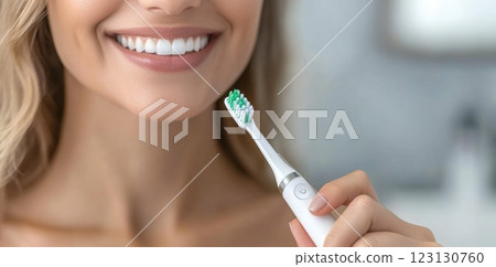 Beautiful woman toothbrush in hand, bathroom setting, electric device, smiling face, personal hygiene, dental care, grooming focus, clean lifestyle, oral health, wellness routine, radiant expression. 123130760