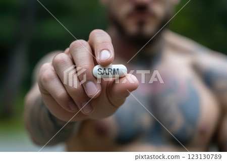 Bodybuilder athlete: SARM pill, muscular physique, fitness dedication, performance boost, disciplined training, supplement regimen, enhanced strength, focused expression, athletic grip, sculpted form. 123130789