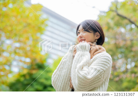 A smiling Japanese woman wearing a white knitwear in the park A smiling Japanese woman wearing a white knitwear in the park 123131307