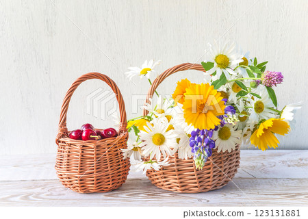 Summer gardening concept: bouquet of various daisies in wicker basket and cherries on white paint wooden background Summer gardening concept: bouquet of various daisies in wicker basket and cherries on white paint wooden background 123131881