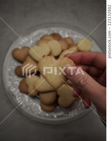 Hand holding heart shaped cookie above plate of valentine's day treats Hand holding heart shaped cookie above plate of valentine's day treats 123132682