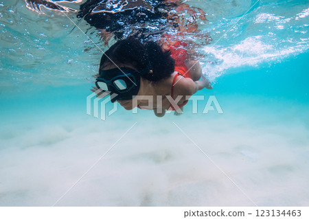 Graceful woman in a swimsuit and mask snorkeling underwater in crystal blue tropical waters with sandy sea bottom 123134463