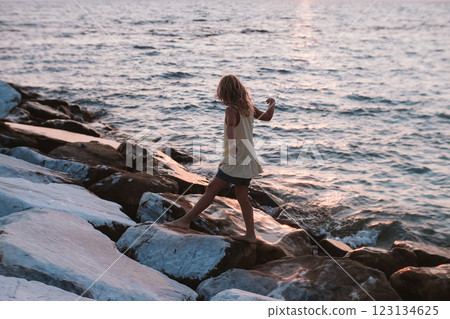 Little blond girl on white stones by sea 123134625