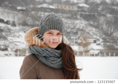 Winter portrait of a smiling woman in snowy landscape wearing grey knit hat and scarf Winter portrait of a smiling woman in snowy landscape wearing grey knit hat and scarf 123135007
