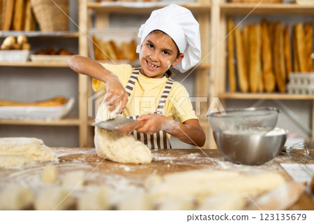 Little girl, baker assistant, cutting raw dough with knife Little girl, baker assistant, cutting raw dough with knife 123135679