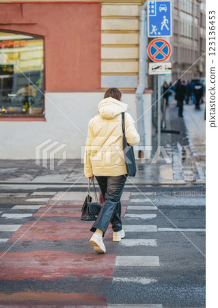 Casual woman crossing street at pedestrian crossing. Woman in white puffer jacket crossing street in an urban setting. Modern fashion, winter clothing, city lifestyle Casual woman crossing street at pedestrian crossing. Woman in white puffer jacket crossing street in an urban setting. Modern fashion, winter clothing, city lifestyle 123136453