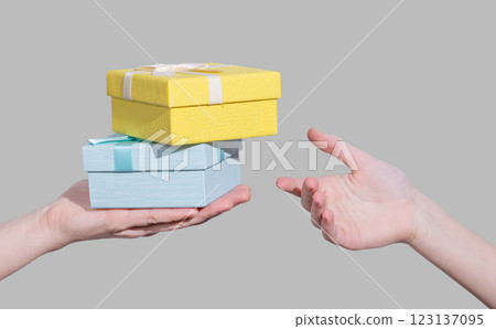Two gift boxes of blue and yellow color in hand on gray background give in other hand. 123137095