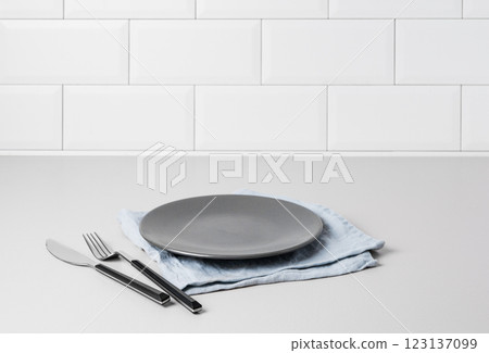 Kitchen countertop with dark breakfast plate, napkin and cutlery on white brick background. 123137099
