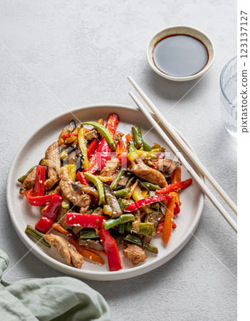 Stir-fry with vegetables and meat on wooden board on white background with chopsticks 123137127