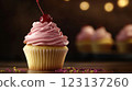 Vanilla cupcake with deep pink frosting and glossy red cherry, moody lighting enhancing golden cake crumb, placed on dark textured wooden backdrop with scattered colorful sprinkles, blurred background 123137260