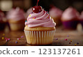 Vanilla cupcake with deep pink frosting and glossy red cherry, moody lighting enhancing golden cake crumb, placed on dark textured wooden backdrop with scattered colorful sprinkles, blurred background 123137261