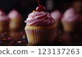 Vanilla cupcake with deep pink frosting and glossy red cherry, moody lighting enhancing golden cake crumb, placed on dark textured wooden backdrop with scattered colorful sprinkles, blurred background 123137263